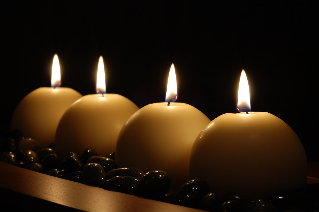 Four lit pillar candles glowing in a dark room