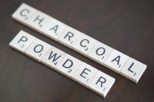 Scrabble tiles spelling charcoal powder on a dark wooden table
