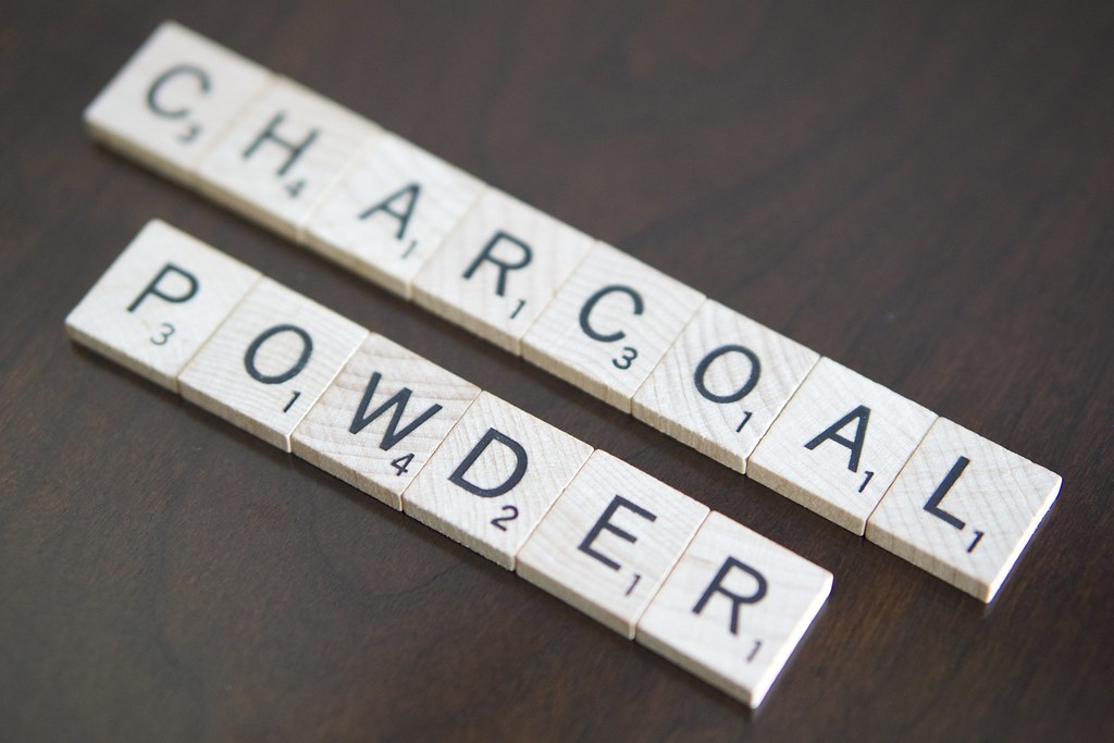 Scrabble tiles spelling charcoal powder on a dark wooden table