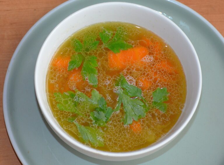 A bowl of clear golden broth with carrots and fresh parsley