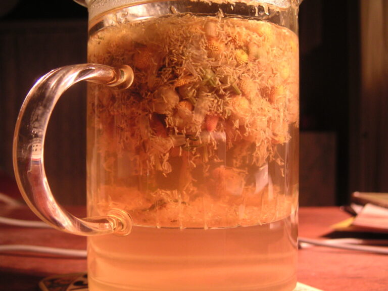A glass mug of chamomile tea with the flowers steeping