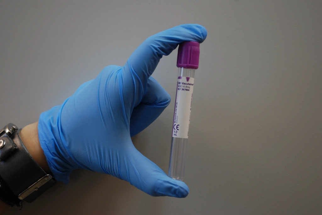 A gloved hand holding a blood collection tube in a lab