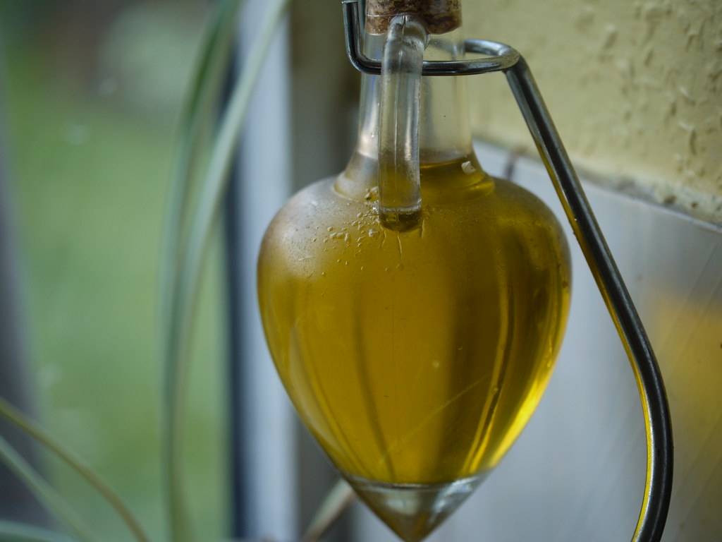 Golden olive oil being poured into a glass jar