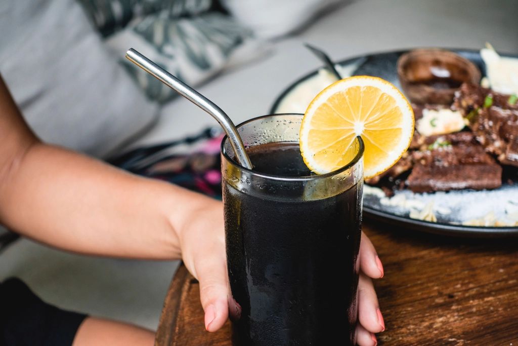 A glass of black lemonade with a lemon slice