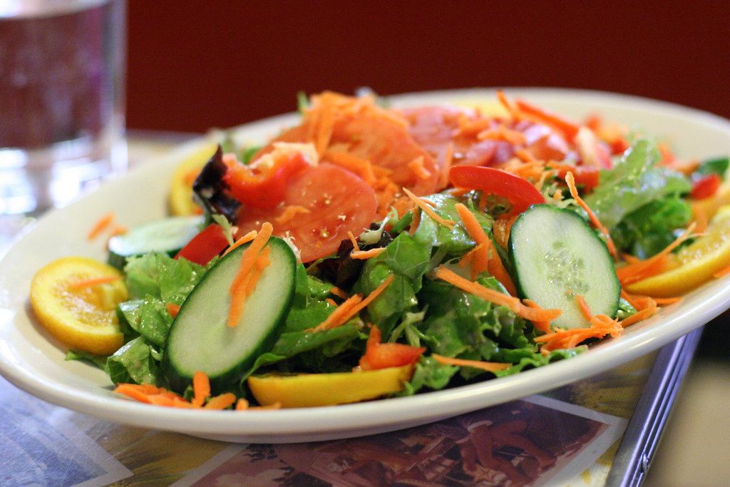 A bowl of mixed salad with greens, tomato and cucumber