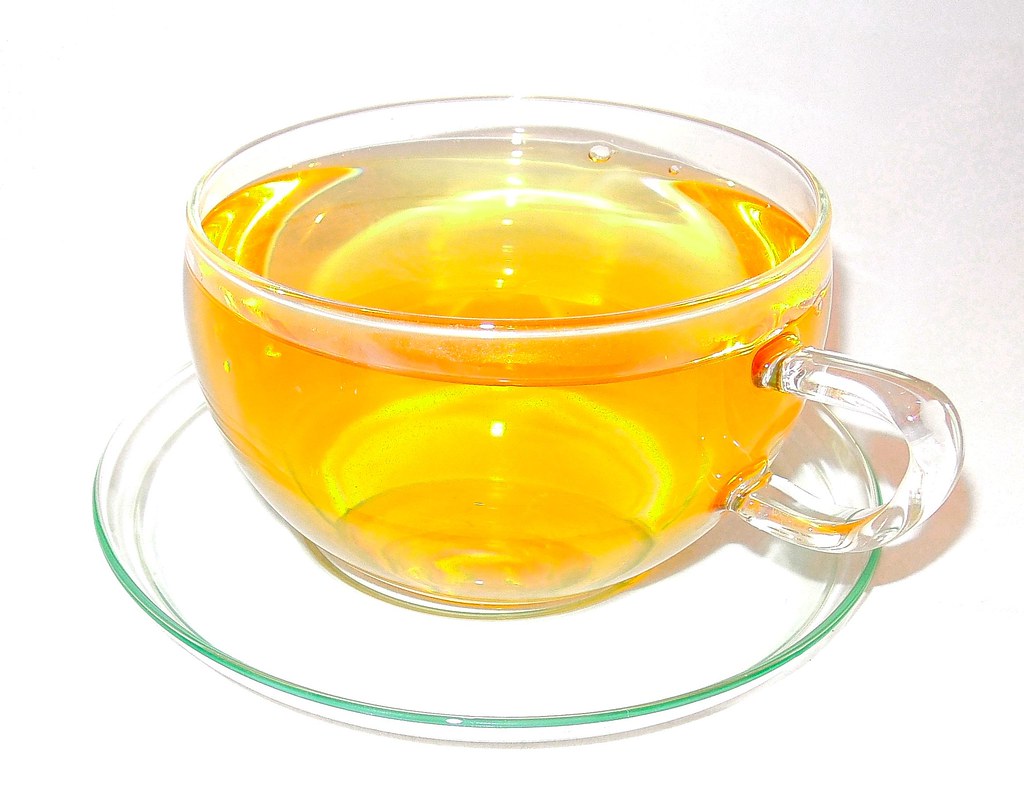 A clear glass cup of pale golden tea on a saucer
