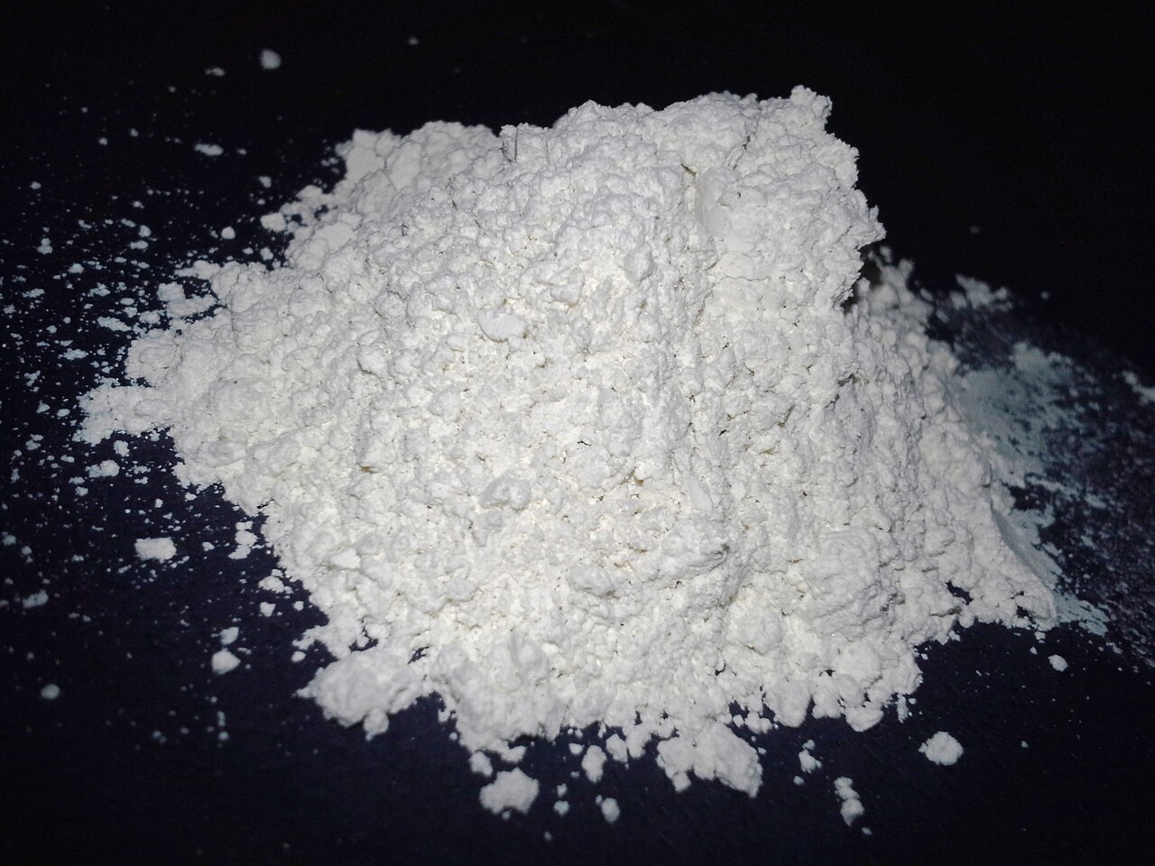 A small heap of white food-grade diatomaceous earth powder on a dark background