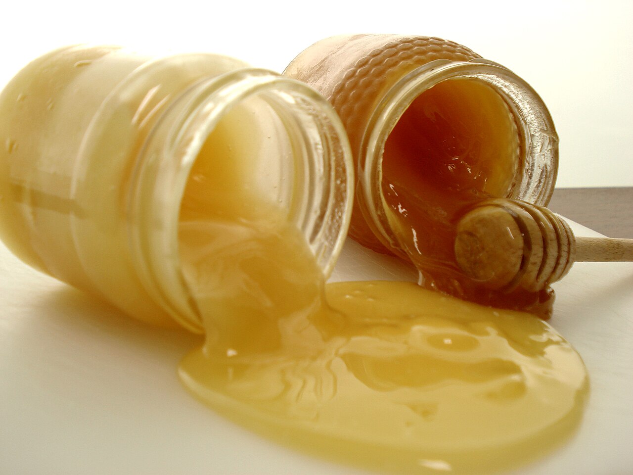 An open jar of thick, raw honey with a wooden honey dipper