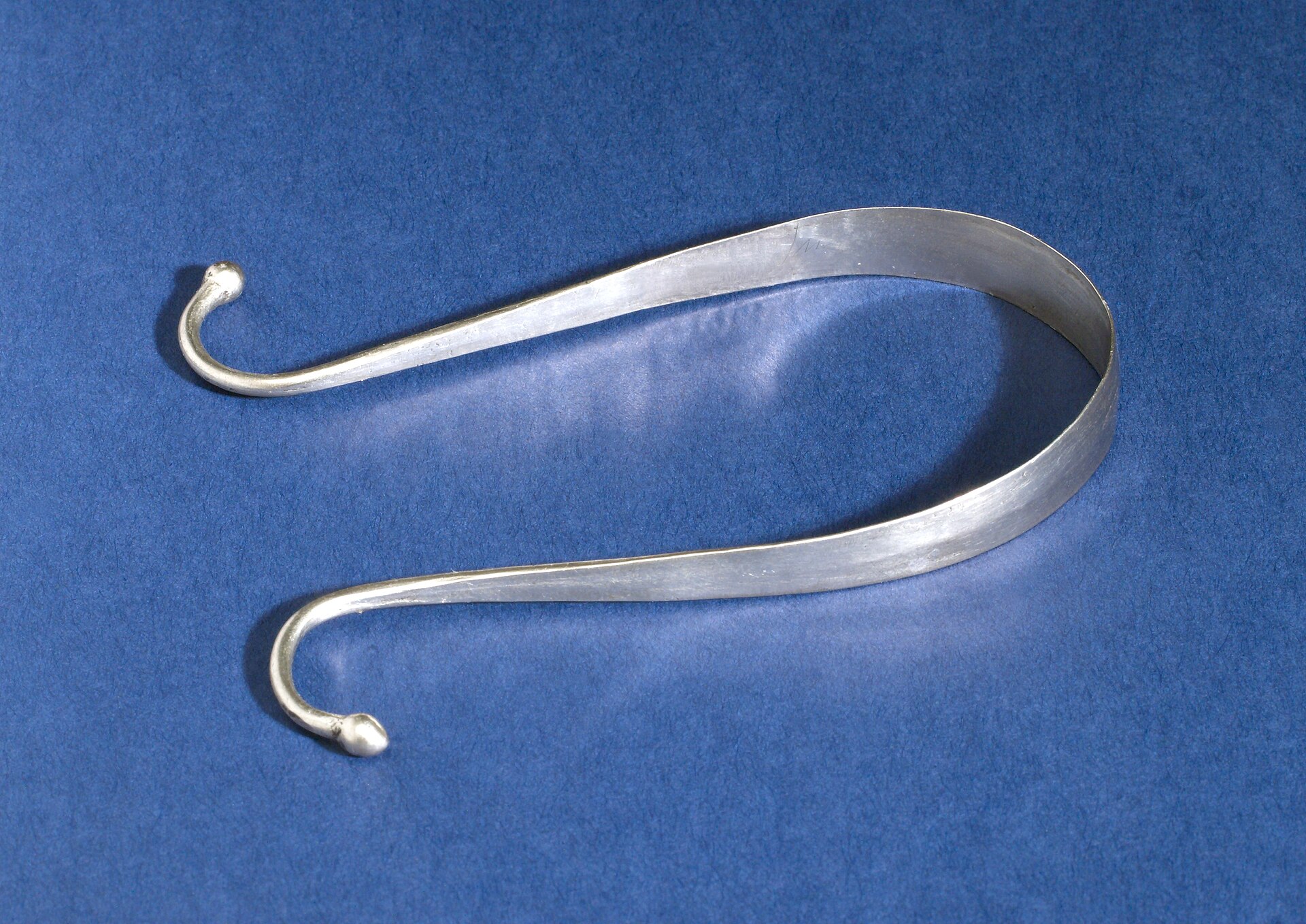 A curved metal U-shaped tongue scraper on a blue background
