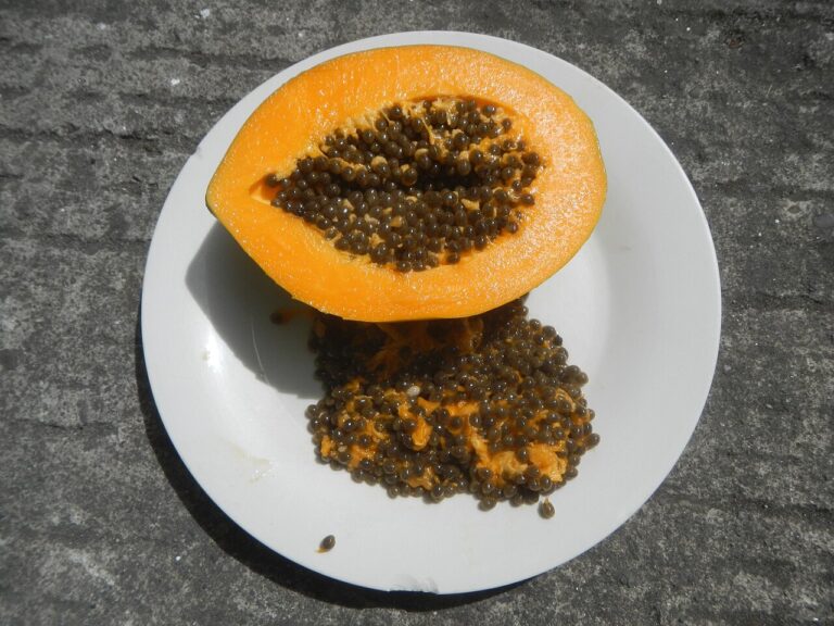 A halved ripe papaya on a white plate with its black seeds scooped out beside it