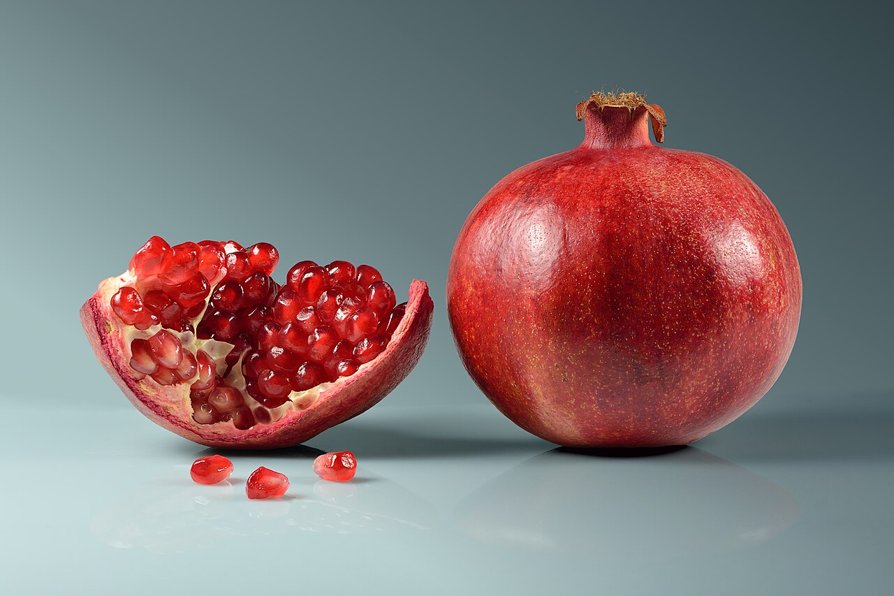 A whole pomegranate beside an opened one showing its red seeds