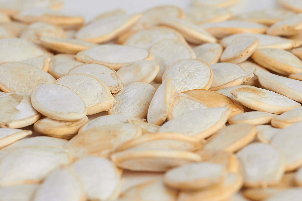A close-up pile of whole, cream-coloured pumpkin seeds