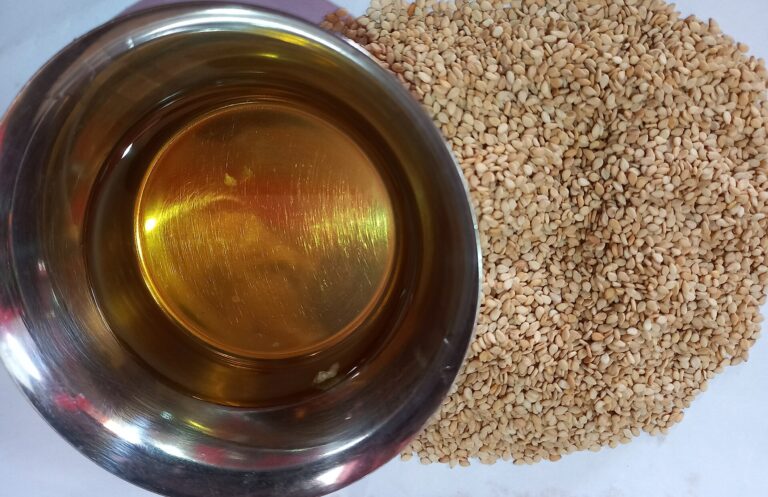 A bowl of golden sesame oil beside a heap of sesame seeds