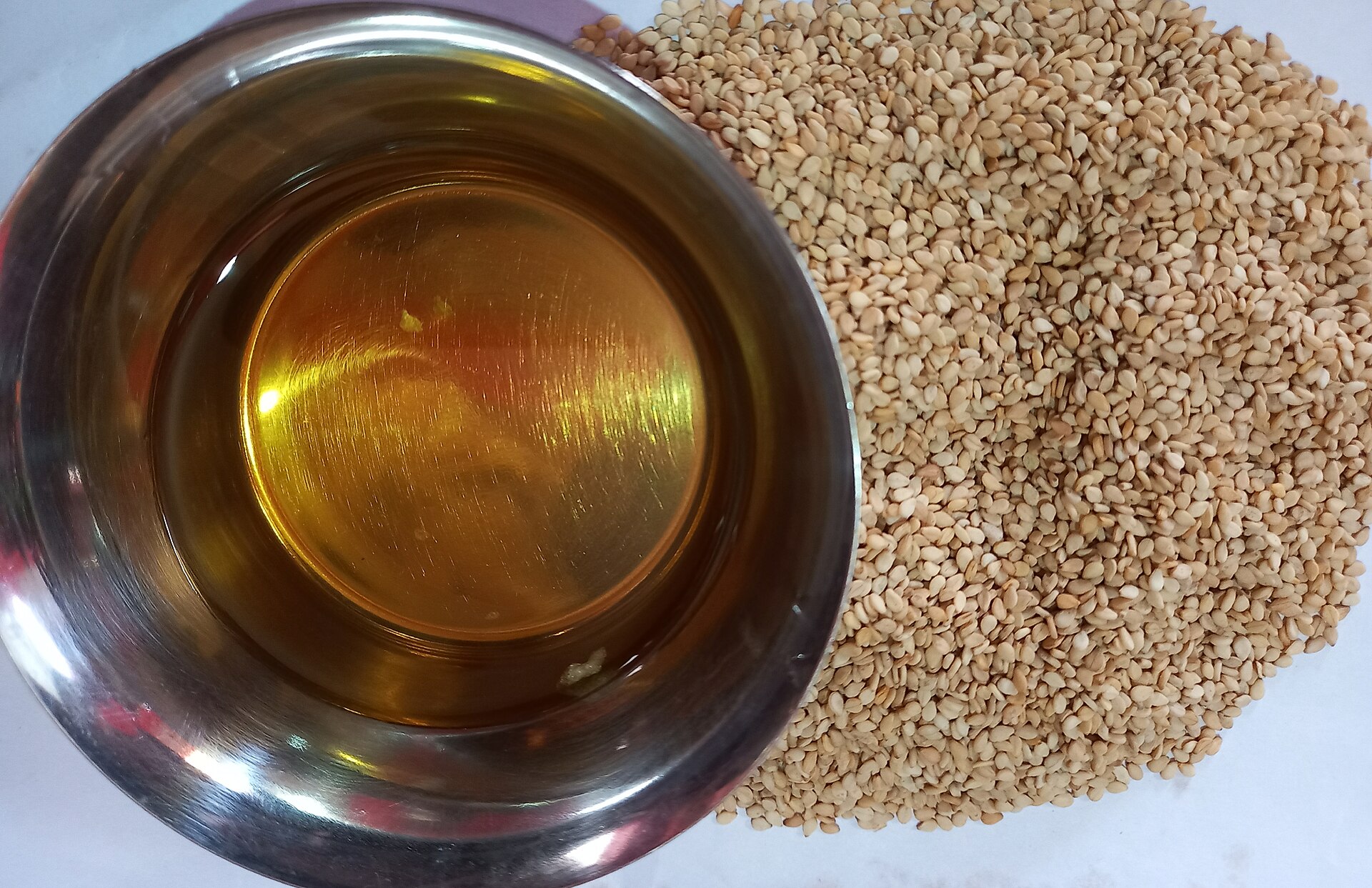 A bowl of golden sesame oil beside a heap of sesame seeds