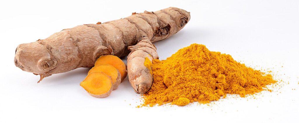 Fresh turmeric roots beside a pile of ground turmeric