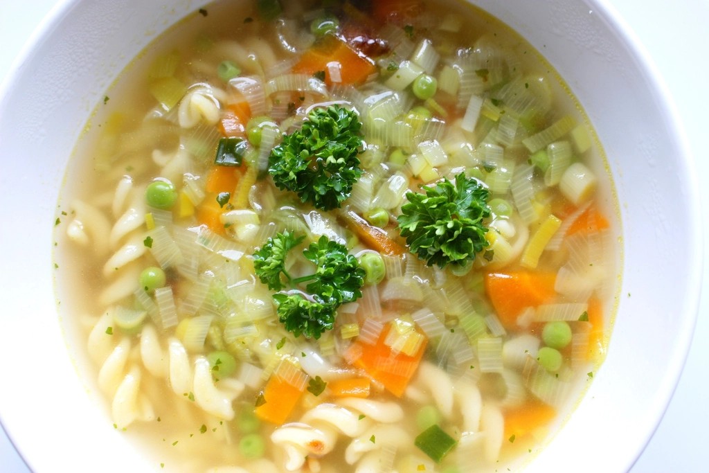 A bowl of vegetable soup with carrots, pasta and fresh parsley